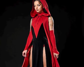 May include: A black velvet gown with high slits and a red hooded cape. The cape has a deep V-neckline and long sleeves. The model is wearing black platform boots. The outfit is set against a black background.