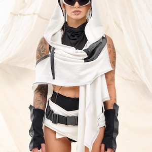K&ouml;nnte beinhalten: Ein futuristisch anmutendes Outfit mit einem wei&szlig;en Kapuzenoberteil mit schwarzen Akzenten, kombiniert mit schwarzen Shorts und einem G&uuml;rtel. Das Ensemble umfasst schwarze Armstulpen und eine Sonnenbrille. Das Outfit hat eine moderne, kantige &Auml;sthetik.