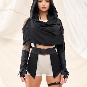 Op de afbeelding: Een zwart hooded top met lange mouwen en een riem. De top heeft een gedrapeerde halslijn en een verkorte lengte. Het model draagt ​​een witte short eronder.