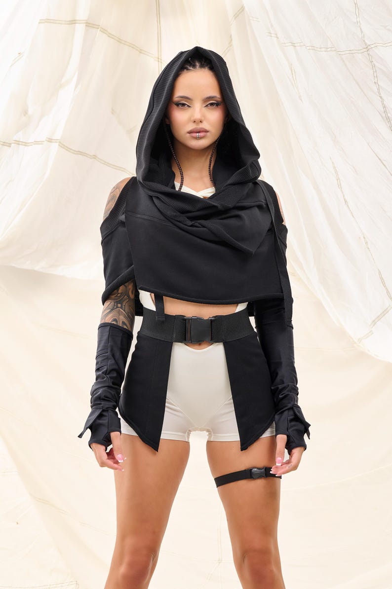 Op de afbeelding: Een zwart hooded top met lange mouwen en een riem. De top heeft een gedrapeerde halslijn en een verkorte lengte. Het model draagt ​​een witte short eronder.