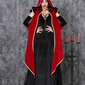 May include: A black velvet dress with a red hooded cape trimmed in gold. The cape is draped over the shoulders. The outfit is accessorized with black gloves and platform boots. A gothic theme.