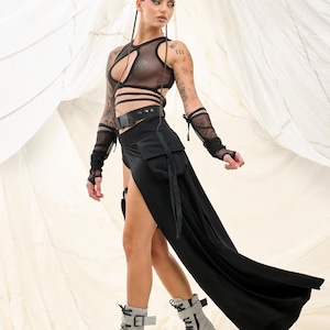May include: A woman wearing a black mesh top with a black belt and a long black skirt with a side slit. She is wearing black lace gloves and grey platform boots with black laces.
