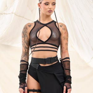 May include: A woman wearing a black mesh crop top with a cut-out design, a black belt, and a black skirt. She is also wearing black mesh gloves and goggles.