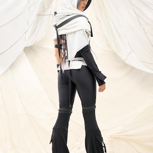 K&ouml;nnte beinhalten: Ein futuristisch anmutendes Outfit mit einem wei&szlig;en Kapuzenoberteil mit schwarzen Akzenten und einem passenden schwarzen Jumpsuit. Der Jumpsuit hat ausgestellte Beine und Taschen. Das Outfit ist modern und edgy gestaltet.