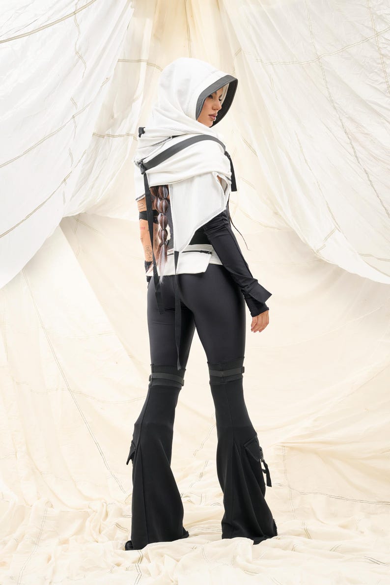 K&ouml;nnte beinhalten: Ein futuristisch anmutendes Outfit mit einem wei&szlig;en Kapuzenoberteil mit schwarzen Akzenten und einem passenden schwarzen Jumpsuit. Der Jumpsuit hat ausgestellte Beine und Taschen. Das Outfit ist modern und edgy gestaltet.