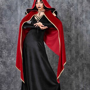May include: A black velvet gown with long sleeves and a matching hooded cape. The cape is red with gold trim. The outfit is a gothic style, suitable for cosplay or themed events.