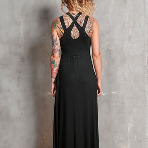 May include: A black maxi dress with a criss-cross strap detail on the back. The dress is sleeveless and has a flowing silhouette.