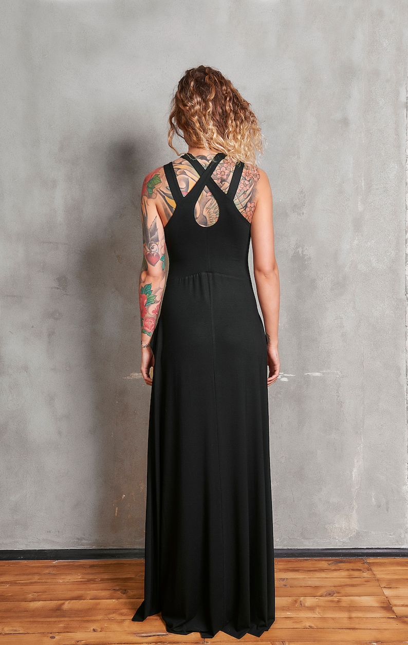 May include: A black maxi dress with a criss-cross strap detail on the back. The dress is sleeveless and has a flowing silhouette.
