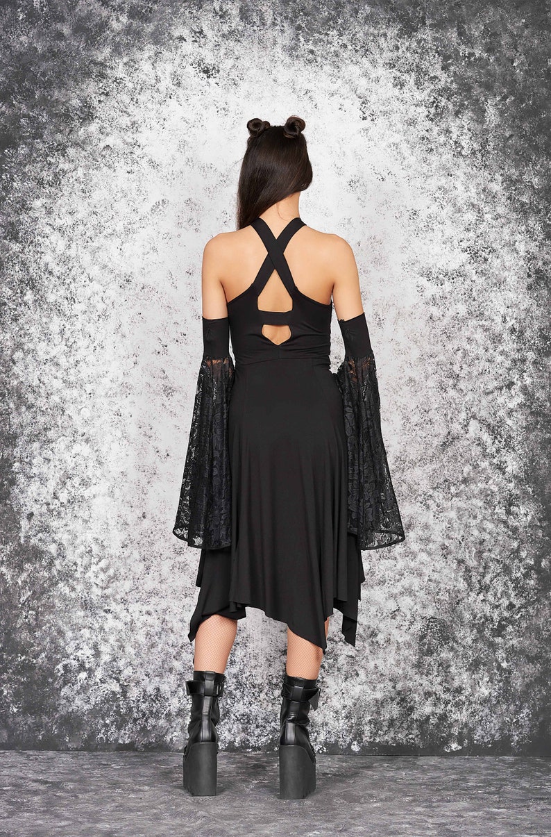 May include: Black dress with a lace overlay and a criss-cross back design. The dress has a flowing skirt and is worn with black platform boots.