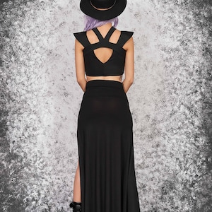 Puede incluir: Conjunto negro de dos piezas con top corto con aberturas en los hombros y falda larga de cintura alta con abertura lateral. La modelo lleva sombrero negro y botas de plataforma. Adecuado para un estilo g&oacute;tico o alternativo.