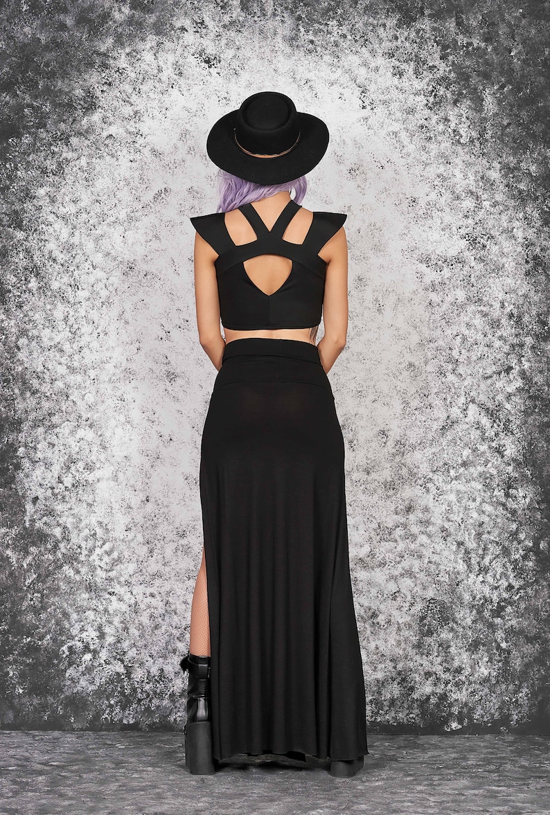 Puede incluir: Conjunto negro de dos piezas con top corto con aberturas en los hombros y falda larga de cintura alta con abertura lateral. La modelo lleva sombrero negro y botas de plataforma. Adecuado para un estilo g&oacute;tico o alternativo.