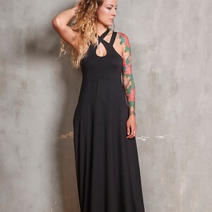 May include: A woman wearing a black maxi dress with a criss-cross halter neckline. She has long, curly blonde hair and a floral tattoo on her arm.