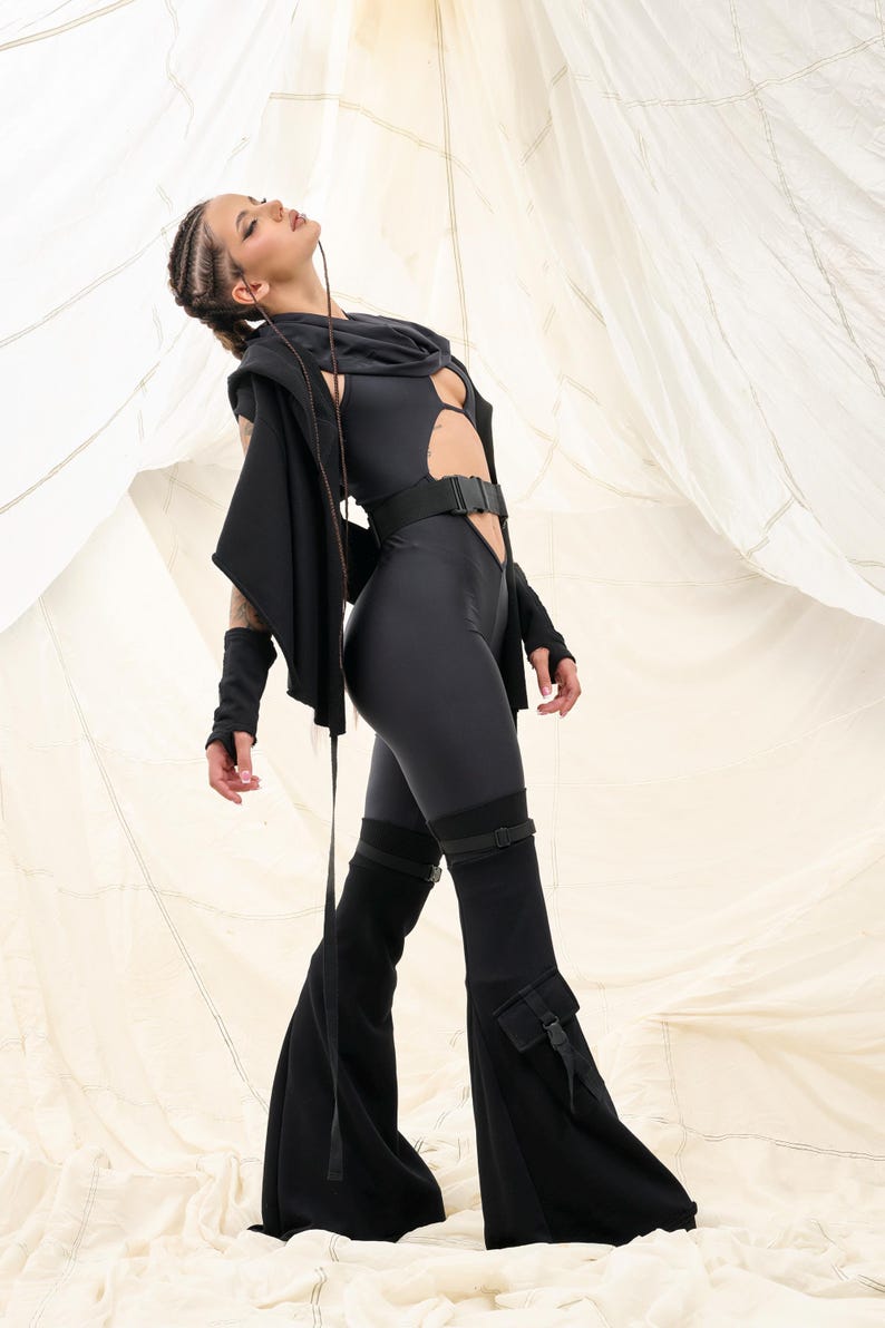 Op de afbeelding: Een zwarte jumpsuit met een uitsparing en een riem. De jumpsuit heeft lange mouwen en wijde pijpen. Het model draagt de jumpsuit met een zwarte hoodie.