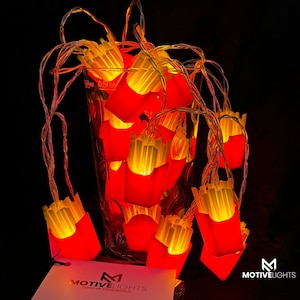 Könnte beinhalten: Lichterkette mit rot-gelben Pommes-frites-förmigen Lichtern. Die Lichter sind auf einem durchsichtigen Draht aufgereiht und in einem durchsichtigen Glas angeordnet. Die Lichter sind vor einem schwarzen Hintergrund beleuchtet. Der Markenname "MotiveLights" ist sichtbar.