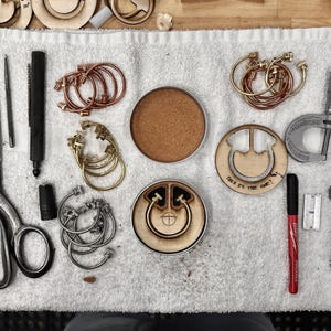 May include: An overhead shot of various craft tools and components, including scissors, a screwdriver, calipers, and several metal rings. Wooden circles and a cork coaster are also present. The text "Take it the one!" is visible on a wooden piece.