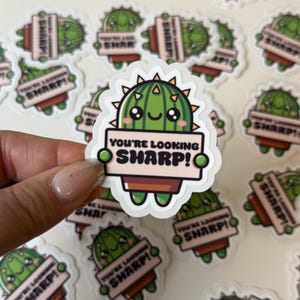 May include: A green cactus cartoon character holding a sign that says "You're looking sharp!" The cactus is wearing a pot and has a happy expression.
