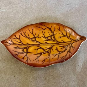 May include: A leaf-shaped decorative dish with a detailed vein pattern. The dish features a gradient of colors, transitioning from a light orange to a darker brown. The edges are outlined in white, creating a defined border. This decorative dish is ideal for home decor.