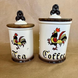 May include: Two ceramic canisters with wooden lids, featuring a rooster design and the words "Tea" and "Coffee".