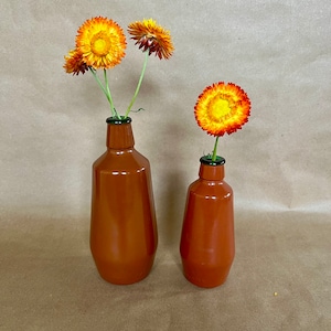 May include: Two terracotta ceramic vases with a green glass top, holding dried orange and yellow flowers.