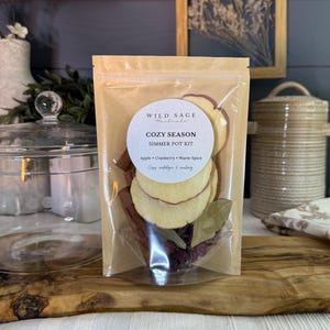 May include: A clear stand-up pouch containing a simmer pot kit labeled Wild Sage Handmade Cozy Season Simmer Pot Kit Apple Cranberry Warm Spice. The kit includes dried apple slices, cinnamon sticks, cranberries, and bay leaves visible inside.