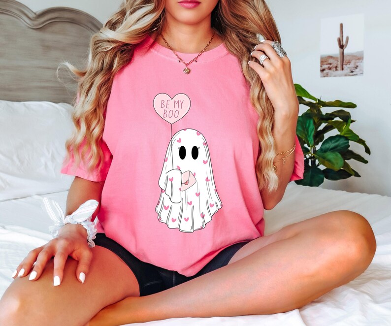 May include: Pink t-shirt with a ghost graphic holding a heart balloon that says "Be My Boo".