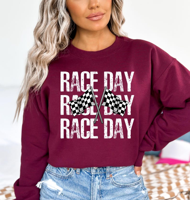 May include: A maroon sweatshirt with the text "RACE DAY" repeated three times. Two checkered flags are crossed in the center of the design.