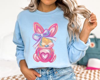 May include: A light blue sweatshirt with a pink and purple cartoon bunny wearing a bow. The bunny is holding a pink heart.
