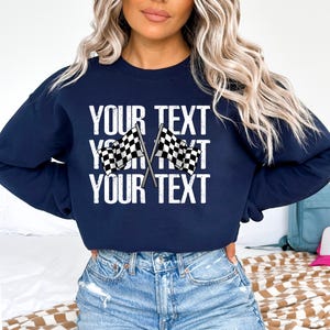 May include: Navy blue sweatshirt with a white graphic of two checkered flags crossed over each other. The text "YOUR TEXT" is repeated three times in a distressed white font.