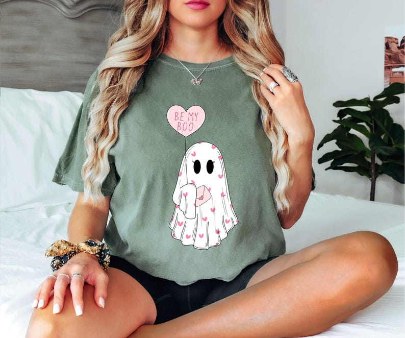 May include: A green t-shirt with a ghost holding a heart balloon that says "Be My Boo". The ghost is covered in pink hearts.