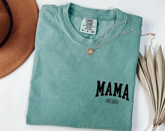 May include: A teal blue t-shirt with the word "MAMA" in black block letters and the text "EST. 2024" underneath.