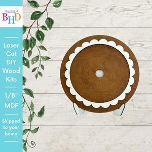 Peut inclure: Kit en bois DIY découpé au laser, marron, avec un bord festonné blanc et deux pieds blancs. Le texte "Laser Cut DIY Wood Kits 1/8" MDF" est visible. Le produit est conçu pour être expédié à domicile.