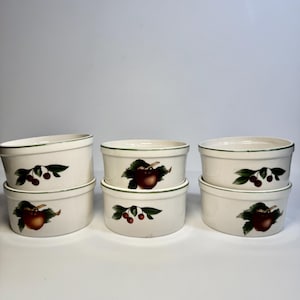 May include: Six white ceramic ramekins with a green rim and fruit illustrations. Each ramekin features a different fruit design, including apples and cherries with green leaves. The ramekins are stacked in pairs.
