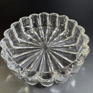 May include: Clear glass decorative bowl with a scalloped edge. The bowl has a starburst design radiating from the center. The glass is thick and has a high level of clarity. The bowl is likely vintage and suitable for display or serving.