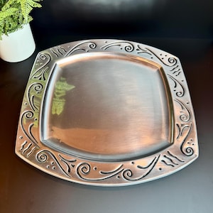 May include: A silver square serving tray with a decorative, embossed, swirling design around the edge.