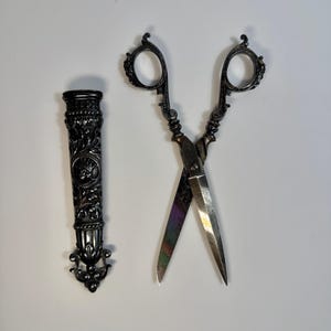 May include: A pair of ornate silver scissors with a decorative handle and a matching silver sheath.