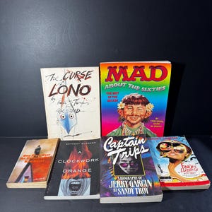May include: A collection of six paperback books with colorful covers. The books include "The Curse of Lono", "Mad About the Sixties", "A Clockwork Orange", "Captain Trips", "One Flew Over the Cuckoo's Nest", and "Fear and Loathing in Las Vegas".