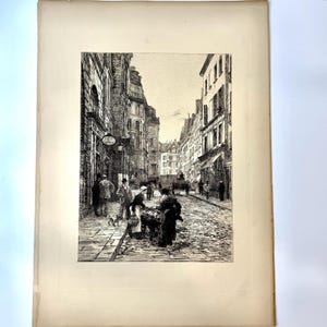 May include: A black and white etching on paper depicting a narrow European street scene with cobblestones, multi-story buildings, and figures in period clothing. A person stands by a cart in the foreground, while others walk nearby.