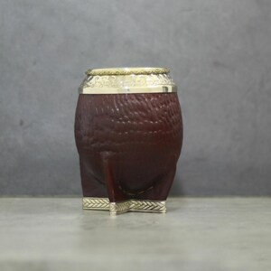 May include: A brown, textured gourd-shaped container with a silver rim and base, and a gold-colored band at the top. The container has three silver legs. The design is a traditional style.
