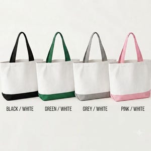May include: Four tote bags arranged in a row, each featuring a white upper section and a colored base with matching handles. The colors from left to right are black, green, grey, and pink. Text labels below each bag read BLACK / WHITE, GREEN / WHITE, GREY / WHITE, and PINK / WHITE.