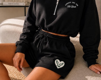 May include: A black two-piece set consisting of a cropped long-sleeve quarter-zip sweatshirt and matching shorts. The sweatshirt features the text "SUNDAYS ARE FOR The Birds" on the chest. The shorts include a heart-shaped patch with an eagle graphic.
