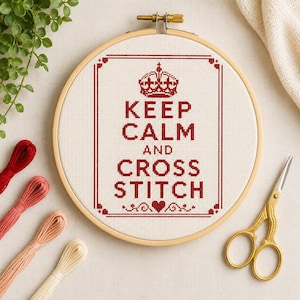 Può includere: Un telaio da ricamo circolare in legno contenente tessuto bianco con un disegno a punto croce rosso. Il testo recita KEEP CALM AND CROSS STITCH, sormontato da un'icona a corona e un cuore in basso. Quattro matasse e forbici dorate.