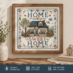 Può includere: Un ricamo a punto croce incorniciato raffigurante una casa con tetto blu, un albero e una staccionata bianca. Il testo HOME SWEET HOME è scritto in lettere blu e rosse. Il disegno è circondato da un bordo decorativo di piccoli cuori rossi e viticci.
