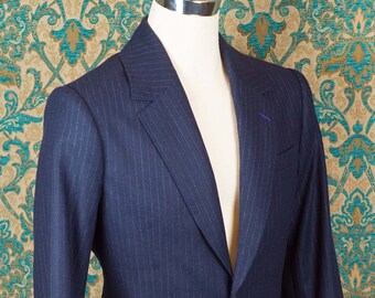 Puede incluir: Una chaqueta azul oscuro de rayas finas con un cierre de un botón. La chaqueta está en un maniquí sobre un fondo estampado.