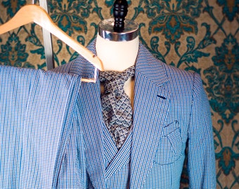 Puede incluir: Un traje azul a cuadros con chaleco y corbata a juego. El traje está en un maniquí y está colgado en una percha de madera.