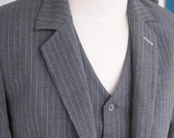 Puede incluir: Una chaqueta de traje gris de rayas finas con un chaleco a juego. La chaqueta tiene solapa de muesca y cierre de un botón. El chaleco tiene cuello en V y tres botones.