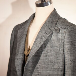 May include: A gray blazer with a textured weave. The blazer is on a mannequin and has a brown vest underneath.