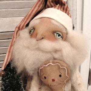 May include: A handmade rag doll Santa Claus with a white beard and a red and white striped hat. He is holding a gingerbread man doll.