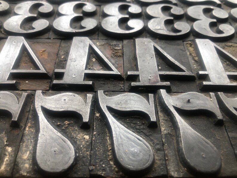 May include: Close-up of metal printing blocks with the numbers 3, 4, and 7. The blocks are arranged in rows and are made of a dark metal with a worn surface.