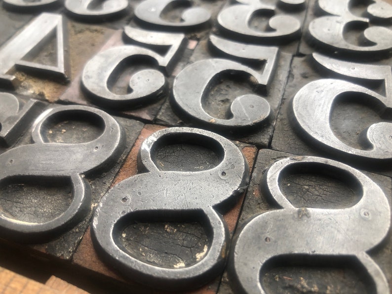May include: Close-up of a set of vintage metal number eight printing blocks. The blocks are made of metal and have a worn, aged look. They are arranged in a random pattern on a wooden surface.