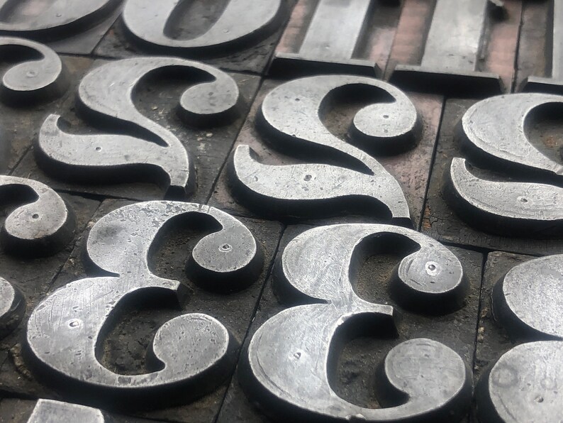 May include: Close-up of a collection of metal letterpress printing blocks, each featuring a different letter of the alphabet. The letters are arranged in a random order, creating a visually interesting pattern.